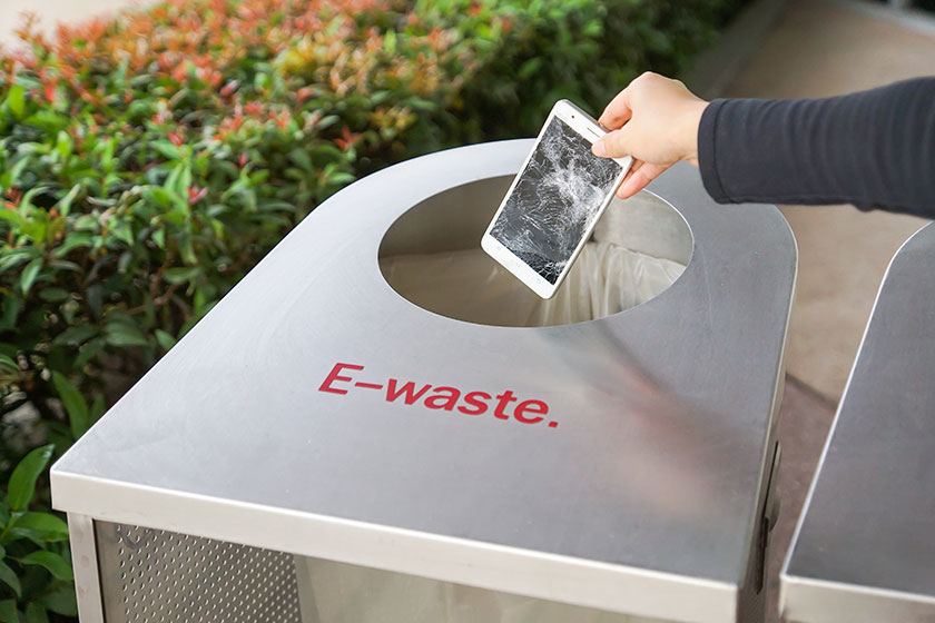 Hand dropping an old, damaged smartphone into a bin for e-waste garbage
